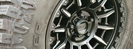 Close-up of a Cooper Discoverer Rugged Trek tire mounted on a black KMC wheel, showing its aggressive hybrid tread and alternating shoulder lugs for on- and off-road traction.