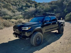 Toyota Tacoma equipped with Yokohama Geolandar MT G003 tires driving off-road, showing aggressive tread blocks and deep sidewall lugs for maximum traction.
