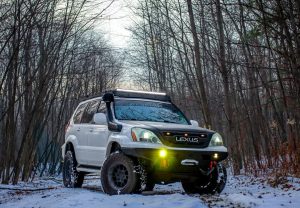 Falken Wildpeak AT4W tires mounted on a Lexus GX driving through a snowy forest trail, highlighting the tire’s aggressive tread and winter-ready traction.