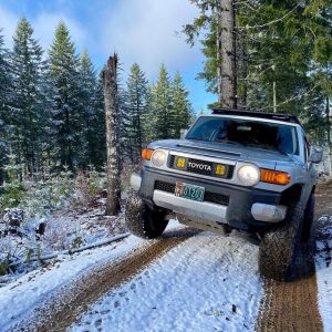 Toyota FJ Cruiser running General Grabber A/TX all-terrain tires in Tillamook State Forest, Oregon, driving through snow-covered off-road terrain.