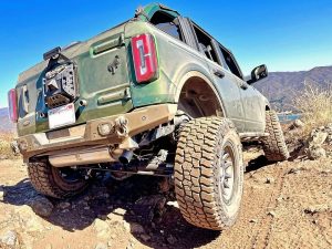 Ford Bronco equipped with Mickey Thompson Baja Boss A/T tires climbing a rocky trail under clear skies, showing aggressive tread pattern and sidewall flex.