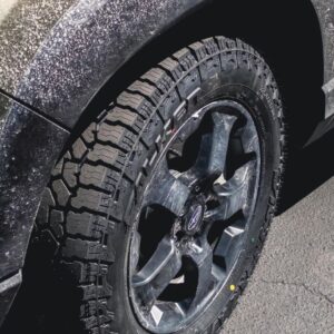 Close-up view of a Subaru wheel fitted with Falken Wildpeak AT4W all-terrain tire, showing aggressive tread design and fresh installation on a slightly dirt-covered fender.