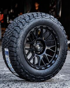Close-up shot of a BFGoodrich All-Terrain T/A KO3 tire mounted on a black multi-spoke alloy wheel, showing detailed tread pattern and sidewall branding.