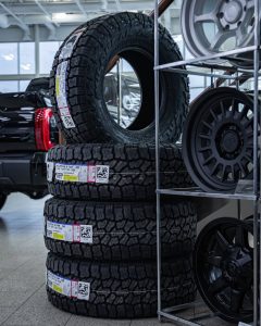 Stack of Falken Wildpeak AT4W HD all-terrain tires labeled LT285/70R17 Load Range E on display beside alloy wheels in an auto showroom.