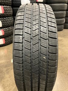 Close-up of Vredestein Pinza HT tire tread showing highway all-season pattern with continuous ribs and deep circumferential grooves for smooth ride and wet traction.